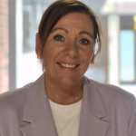 Portrettbilde Monica T. Melvold. Smilende, mørkt hår samlet i hestehale, beige blazer, hvit topp.