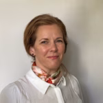 Profilbilde Kristin Bruvik, brunt hår satt opp i lav hestehale, hvit skjorte og fargerikt silkeskjerf rundt halsen, rød leppestift