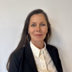 Portrettbilde av Siv Bjønnum, mørkebrunt langt hår, rød leppestift, hvit bluse, svart blazer, smilende.
