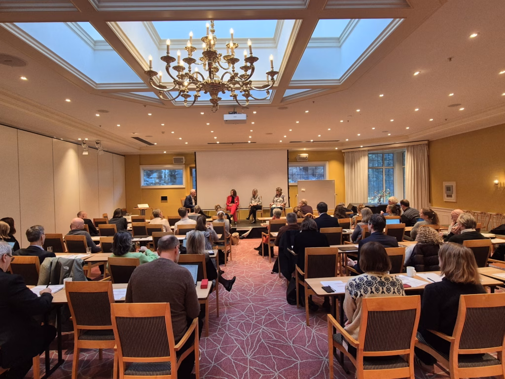 Bilde av fullsatt sal under den nasjonale dialogkonferansen, tatt fra bak i salen slik at man ser mot scenen under en panelsamtale.