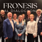 Bilde av 8 av prosjektgruppemedlemmene oppstilt inntil hverandre på to rekker. Svart gradiert bakgrunn over i grått, med teksten "FRONESIS Nasjonal dialogkonferanse"
