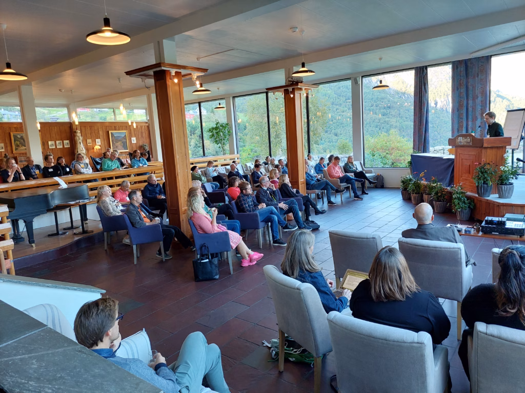 Bilde av fullsatt sal under "The First Nordic Conference on Medical Workplace Learning" på Stalheim hotel i 2023. Flott sal med store søyler og vinduer ut mot vakker grønn natur og fjell.