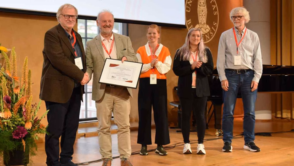 Bilde av prisvinnere sammen med prisutdeler på scenen. Utdeling av diplom, og applaus.